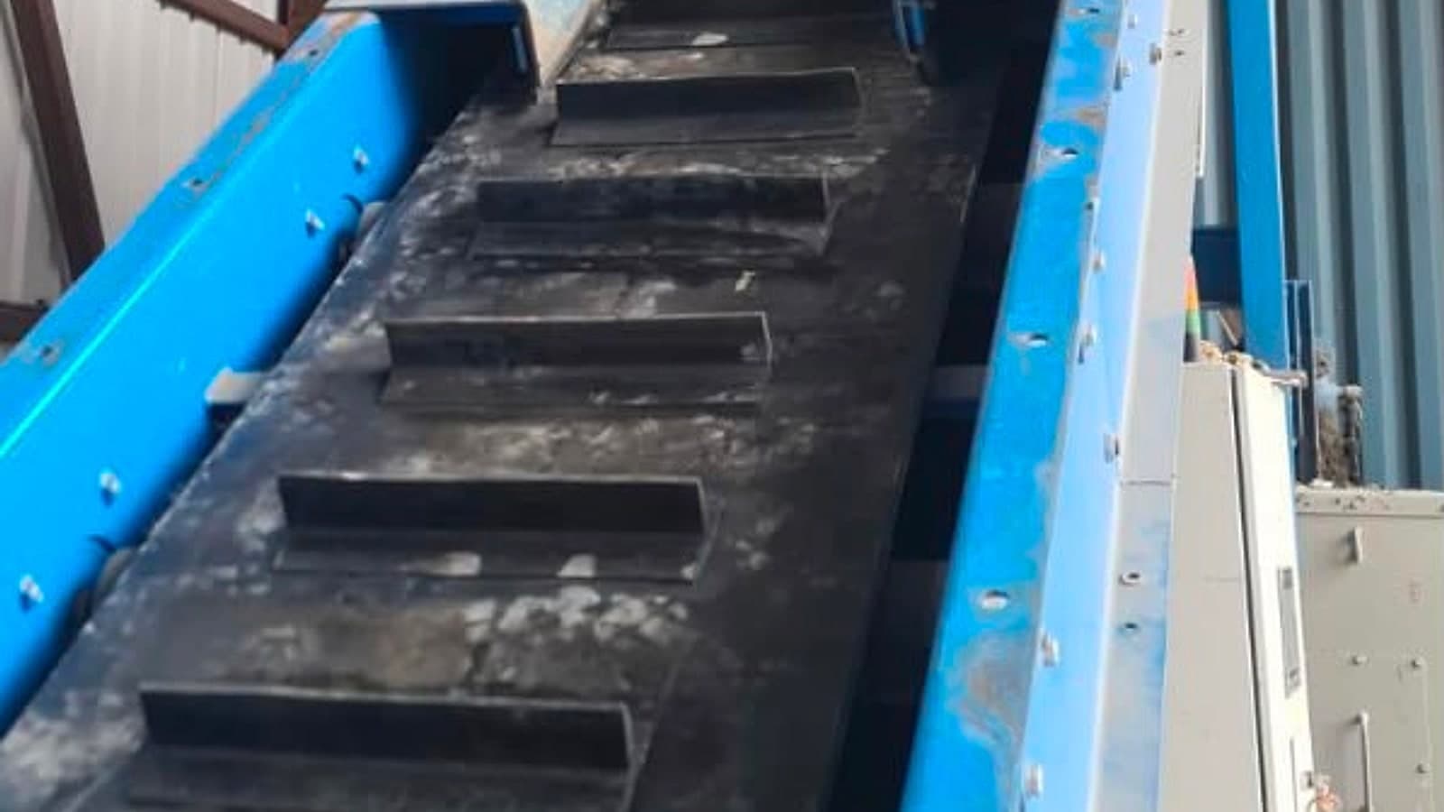 Cleated belt running up a steep incline conveyor inside a recycling plant
